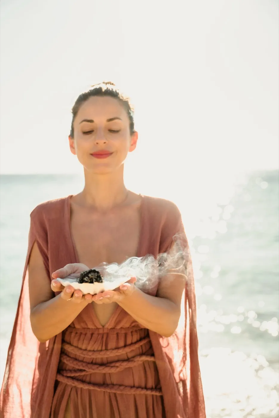 Dalia by the sea, eyes closed, holding a shell with smoking herbs